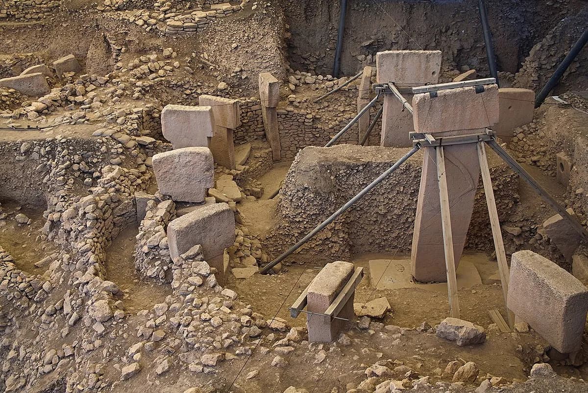 Kazı alanında taş duvarlarla çevrili yuvarlak bir yapı; ortada metal desteklerle tutulan uzun, T biçimli bir dikilitaş, çevresinde duvara gömülü daha küçük taşlar